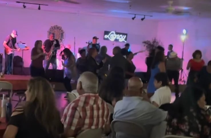 Live band performing on stage with purple lighting as audience members watch from the floor in an indoor venue