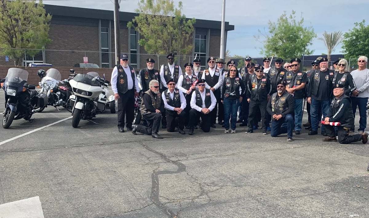 Large group of people in black vests and motorcycles gathered in a parking lot outside a brick building