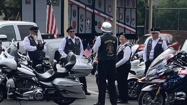 Group of motorcyclists in vests gathered near motorcycles outside a building with American flag