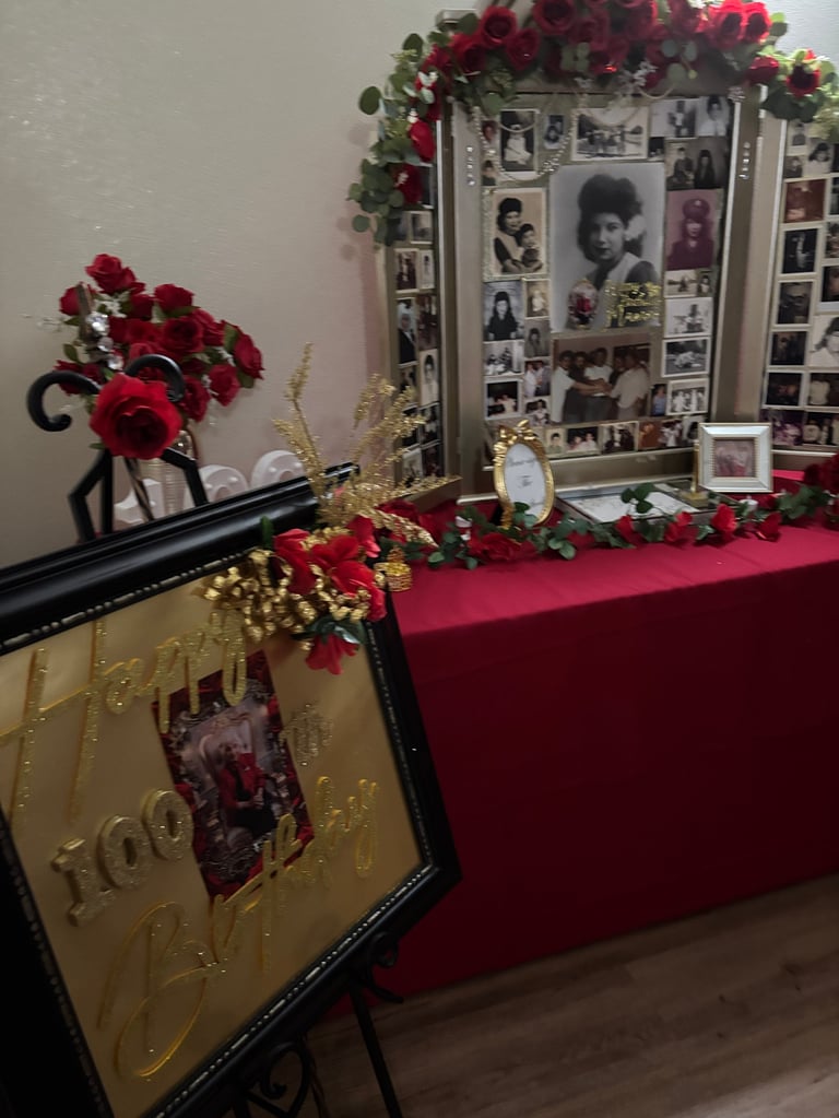 Memorial display with red roses, framed photos on wall, gold decorative panel, and red draped table