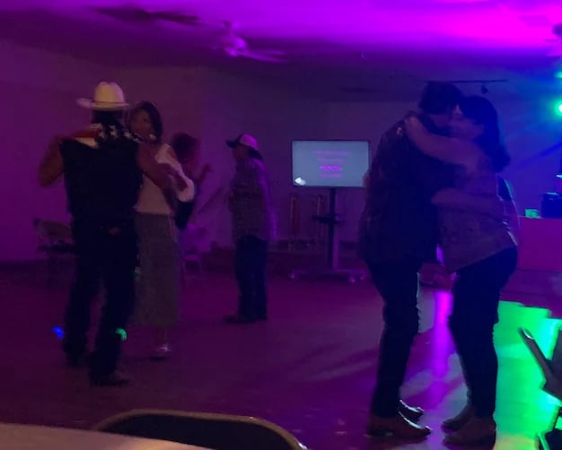 People dancing and socializing in a dimly lit venue with purple and neon green lighting and a screen in the background