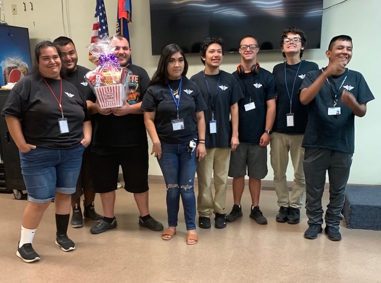 Group of eight people wearing matching black shirts and lanyards standing together indoors with American flags and popcorn decoration visible in background