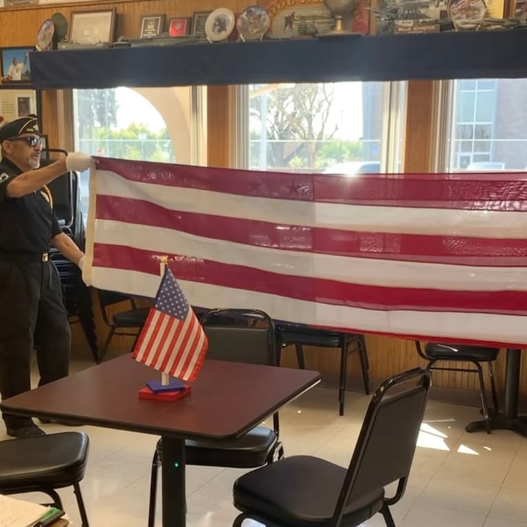 Person holding large American flag in room with small flag on table and decorative items on shelves