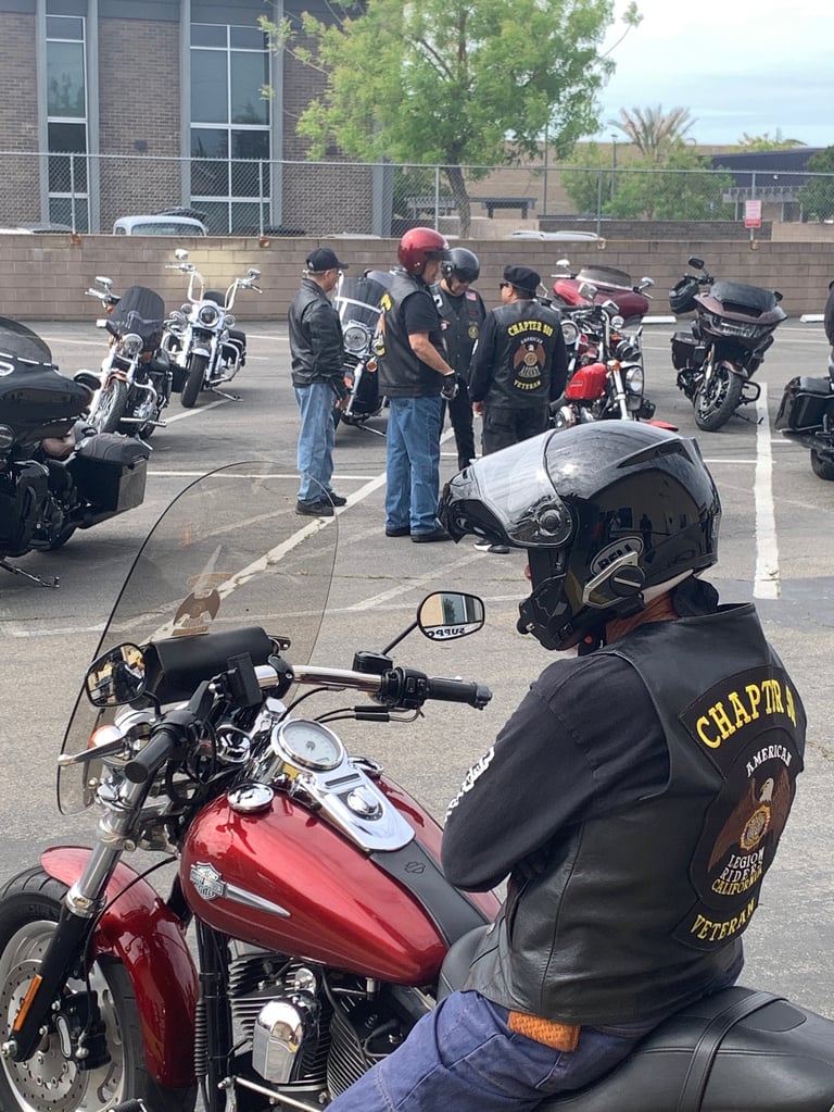 Motorcycle gathering in parking lot with riders in leather jackets and various Harley-Davidson style bikes