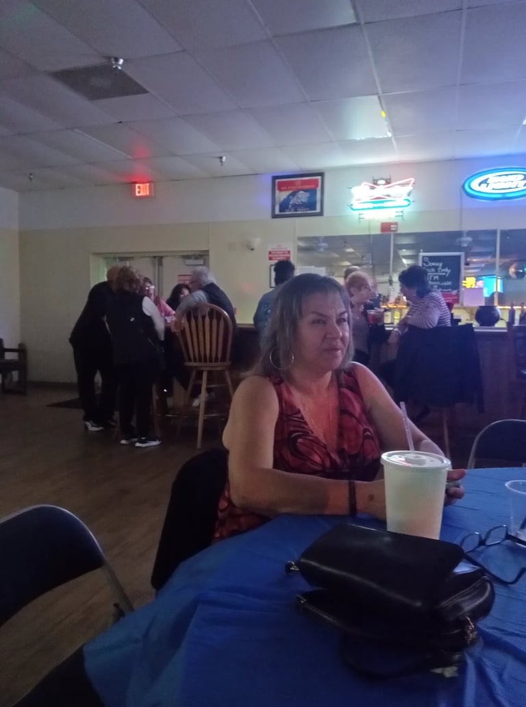 Woman in red top sitting at blue table in casual indoor venue with other guests and neon signs in background