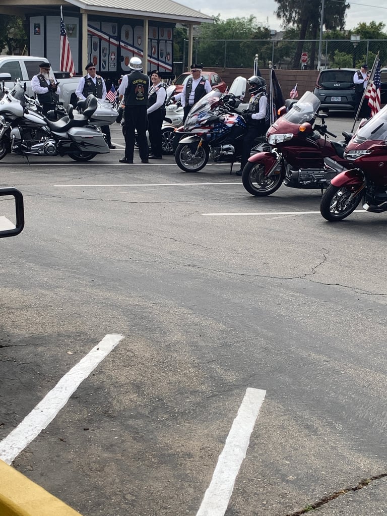 Motorcycle riders gathered in parking lot for rally, American flags visible, motorcycles lined up