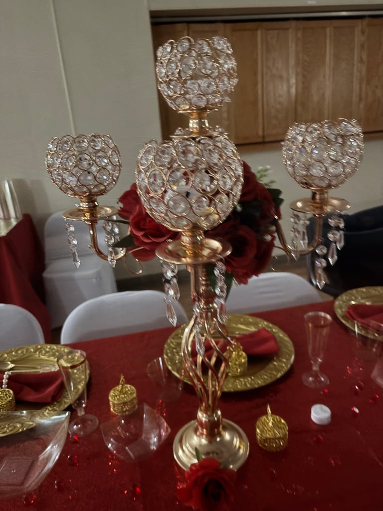 Elegant gold candelabra with crystal beaded shades and red roses on a formal red table setting with gold accents