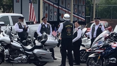 Group of motorcyclists gathered outside a biker clubhouse with parked motorcycles and an American flag