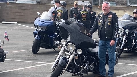 Motorcycle club members in leather vests gather in a parking lot with custom cruiser motorcycles
