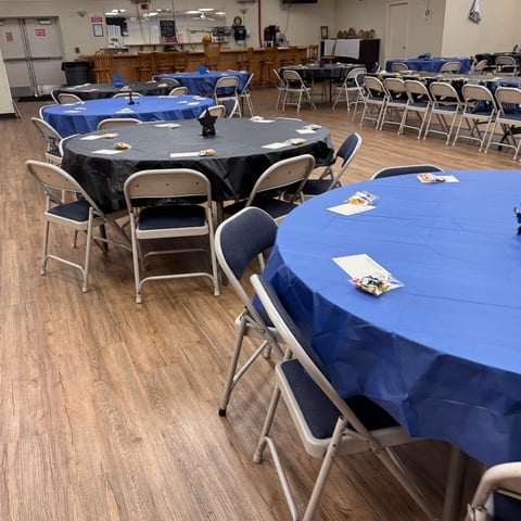 Community hall with round tables covered in blue tablecloths and folding chairs arranged for an event