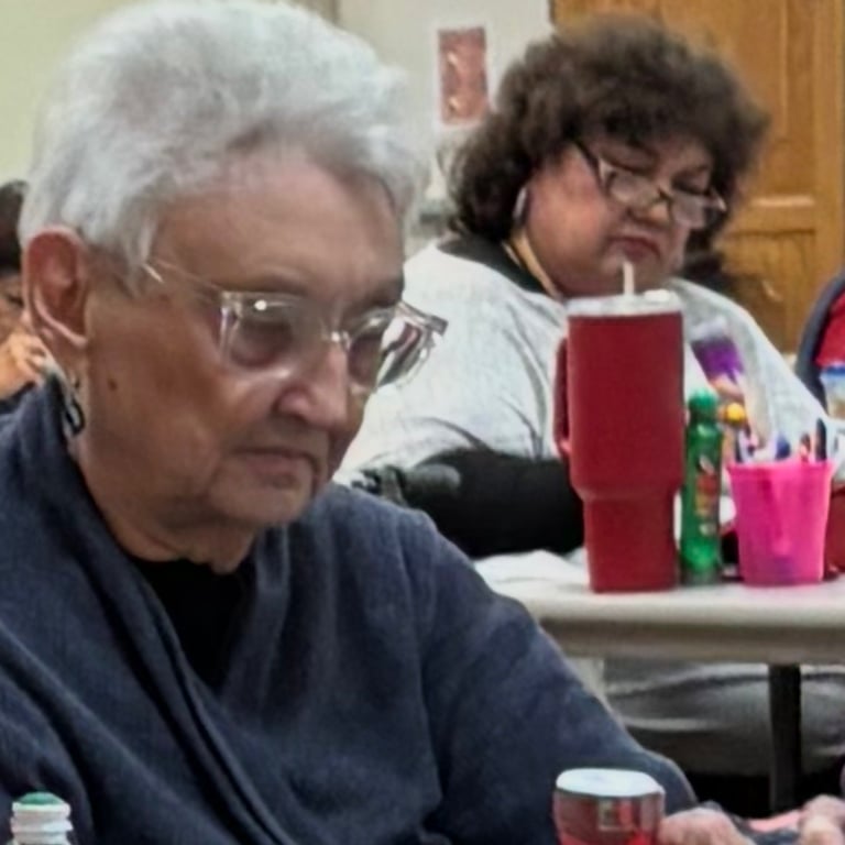 Two seniors sitting at a table with drinks and candles, appearing to be at a community or religious gathering indoors