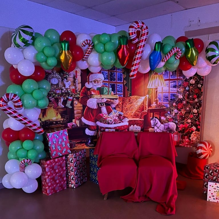 Festive Christmas display with red velvet couch, colorful balloon garland, candy canes, wrapped gifts, and illuminated holiday decorations