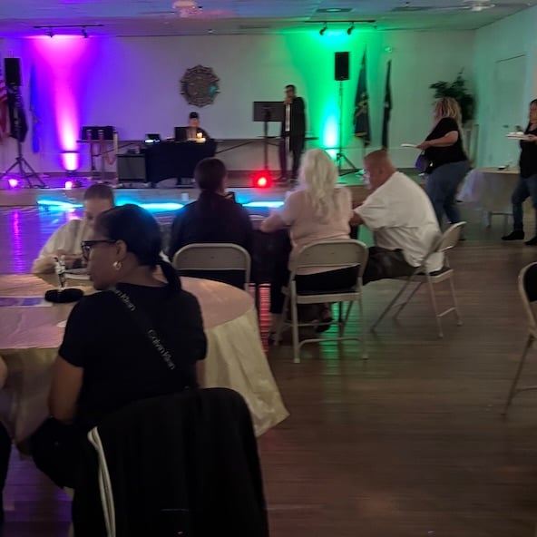 Event venue with guests seated around tables under colorful purple and green ambient lighting during an indoor celebration or party