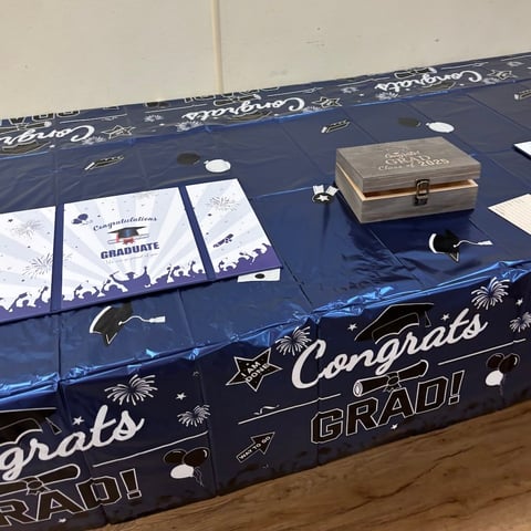 Graduation party table decorated with blue tablecloth, congratulations cards, and a gold gift box