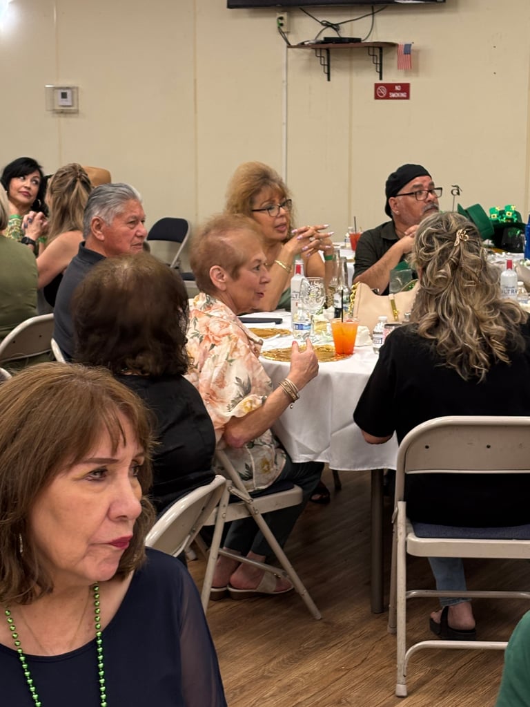 Group of adults seated at tables during an indoor gathering or meeting, with drinks and food visible