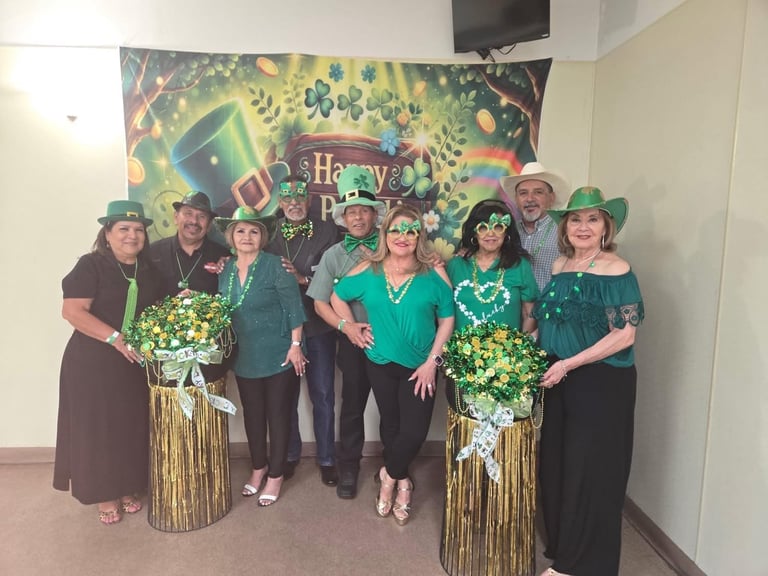 Group of people wearing green and festive hats posing together indoors with holiday decorations and large floral arrangements behind them