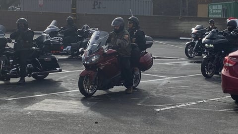 Group of motorcyclists gathered in parking lot, with riders on maroon and black motorcycles